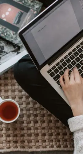 Crop young businesswoman using laptop while drinking tea at home