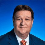 A man in a suit and tie is posing against a blue background.