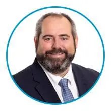 A man with a beard in a suit and tie is smiling.