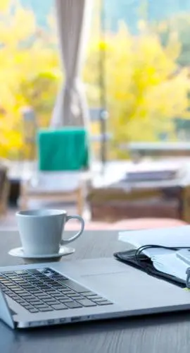 Cozy workplace of freelance occupation person with portable computer coffee notepad located on wooden table in suburban cottage terrace