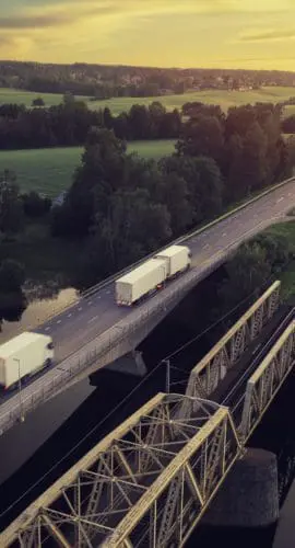 Two trucks with trailers on the road at sunset through a rural landscape in the Dalarna region of Sweden.