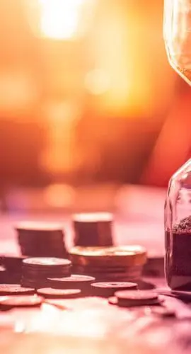 Sand running through the shape of hourglass on table with banknotes and coins of international currency. Time investment and retirement saving. Urgency countdown timer for business deadline concept