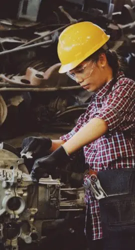 Woman wears yellow hard hat holding vehicle part