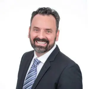 A man in a suit with a striped tie is smiling against a plain white background.