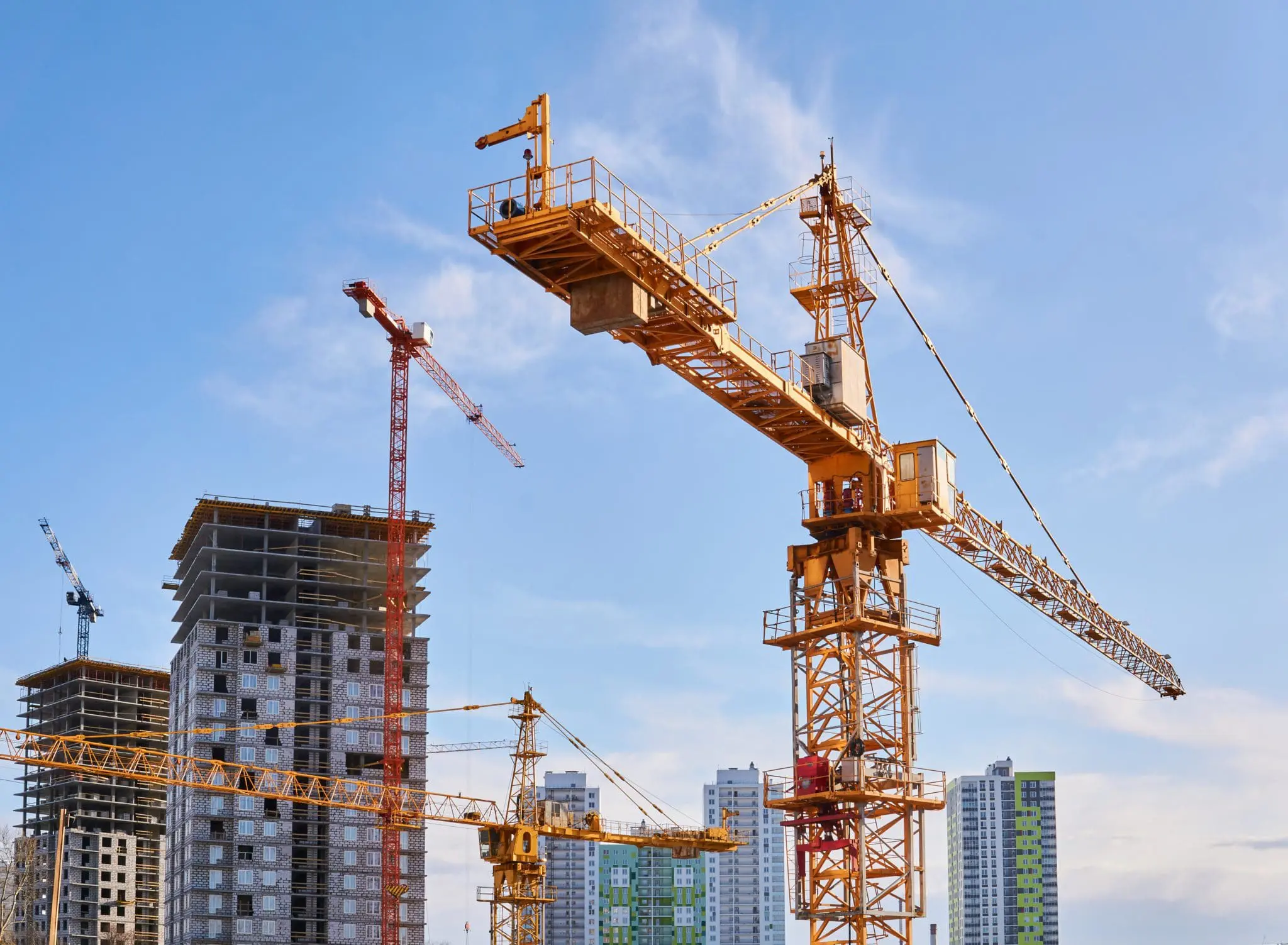 several construction tower cranes of different heights at a building site during the construction of blocks of flats, view against the sky