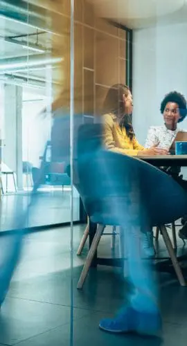 Businesspeople in Conference Room and Colleagues Walking By. Blurred motion of colleagues walking briskly down office hallway as colleagues sit in conference room discussing ideas. Busy modern workplace. Working process in the office, business people working, walking and talking, blurred motion