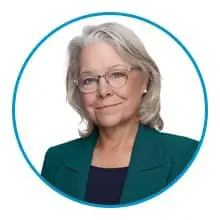 A person with gray hair and glasses is wearing a green blazer against a white background.