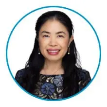 A person with long dark hair, wearing a dark floral top, and smiling against a white background encircled by a blue border.