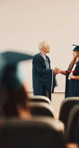 Happy senior professor shaking hands with her graduate students in a lecture hall. Copy space.