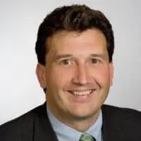 A smiling individual with short brown hair is wearing a suit and a green tie.