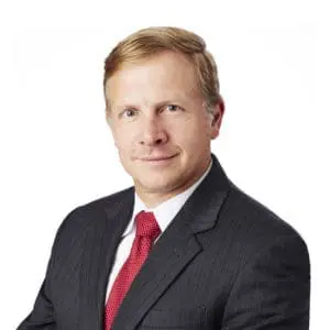 A person wearing a dark suit, white shirt, and red tie poses against a plain white background.