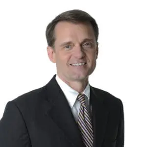 A person in a suit and tie is smiling against a white background.