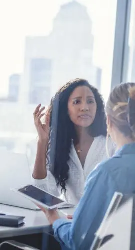 Business colleagues having a conversation. They are both young business people casually dressed in a modern office. Could be an interview or consultant working with a client. One woman looks upset, she could be getting fired. One person has her back to us. Mixed ethnic group. One is African American and the other is Caucasian