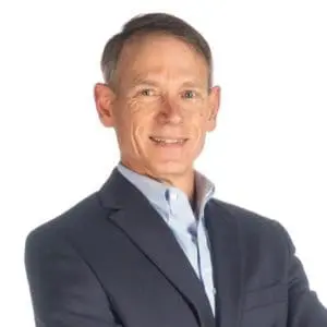 A person is wearing a suit and smiling at the camera with a relaxed posture.