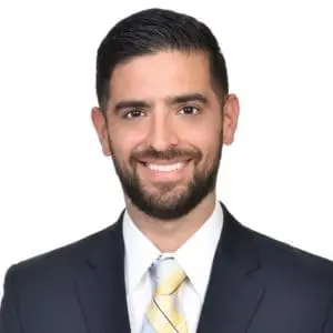 A smiling man in a suit and tie is posed against a plain white background.