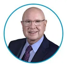 A man with glasses and a bald head is wearing a suit and tie, smiling within a circular blue border.