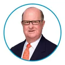 A man wearing glasses and a suit with an orange tie is depicted within a blue circular border.