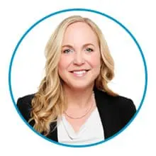 A person with long blonde hair, wearing a black blazer over a white top, smiles against a white background framed by a blue circle.