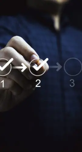 Hand checking off steps on a due diligence checklist, representing stages in a sale-leaseback transaction for real estate investors