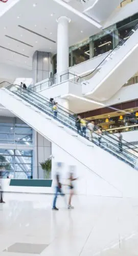 Modern shopping mall interior with escalators and retail storefronts, representing commercial real estate and retail center financing.