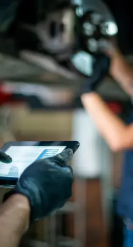 Focus on foreground of engineer holding a tablet checking the readings of the carâs sensor while the mechanic adjusts them on the disk - Car industry concepts