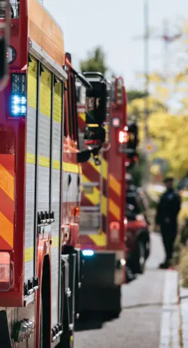 Red fire trucks in row. Teams of fire brigade on city street. Selective on blue flasher.