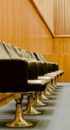 A modern jury box in a Federal bankruptcy court. Jurors’ area in courtroom consists of a single row of black leather swivel chairs with LCD computer monitors mounted on a partition in front of them intended for evidence viewing. A microphone stands on the opposite side of the partition in the wood paneled court room.Another image in this series: