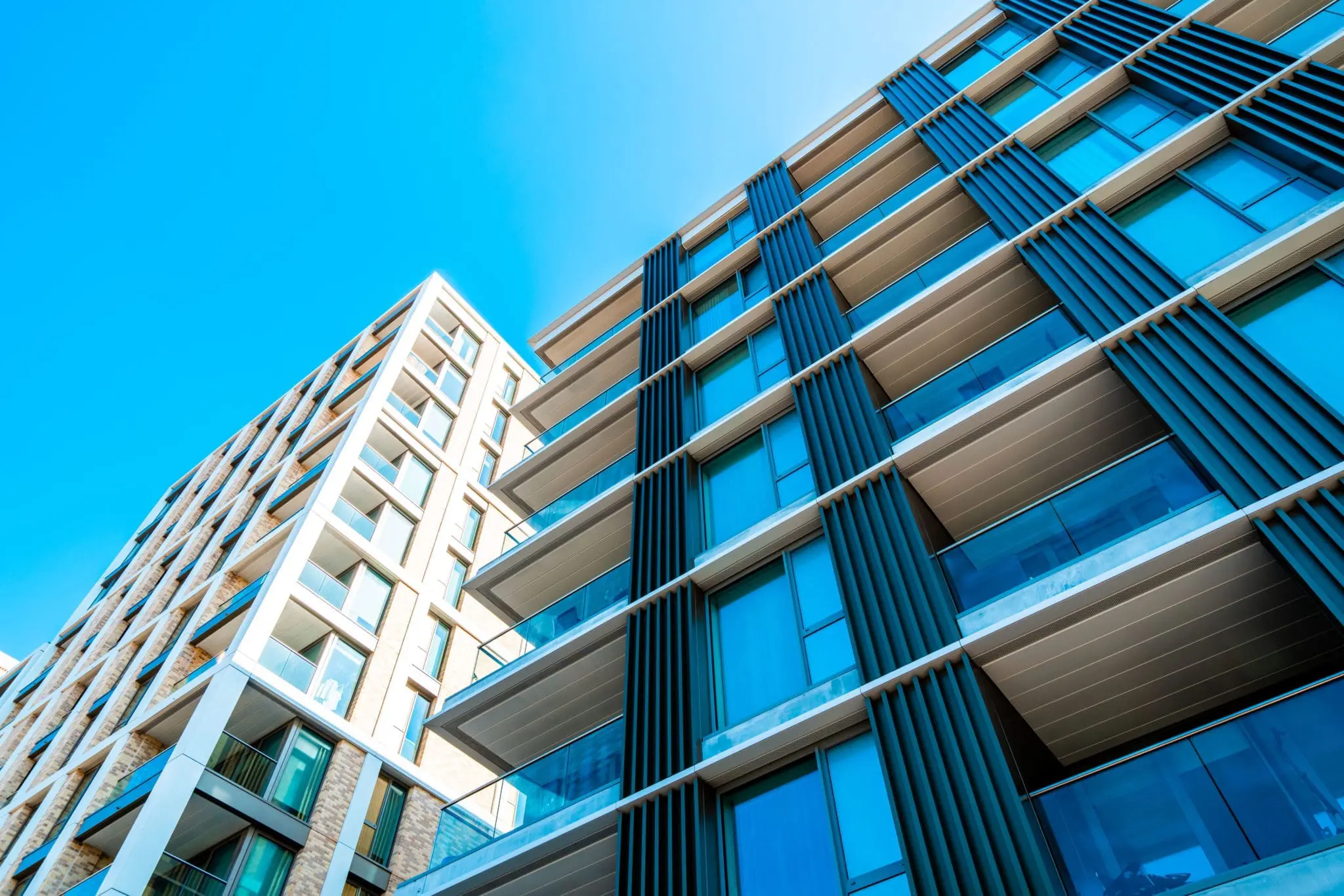 Modern multifamily apartment buildings photographed from ground level against a clear blue sky, representing affordable housing and real estate development