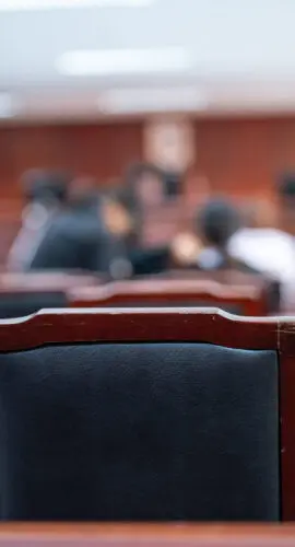 A classroom with a black chair in the foreground. The chair is empty and the room is filled with people