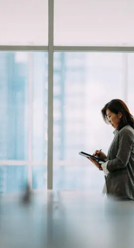 An Asian businesswoman holding digital tablet and  look in distance window thinking or planning future success, thoughtful motivated mature businesswoman pondering over new ideas.