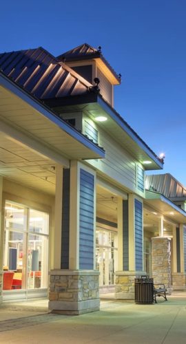 A row of illuminated storefronts under a dusk sky.