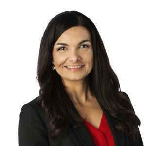 A smiling woman with long dark hair wearing a black blazer over a red top.