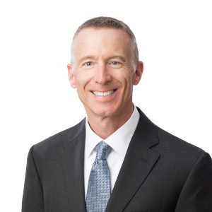 A smiling man wearing a suit and tie against a white background.