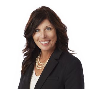 A smiling woman with dark hair wearing a black blazer over a white top and a pearl necklace.