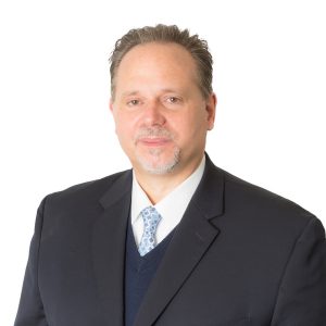 A person wearing a business suit with a tie poses against a white background.