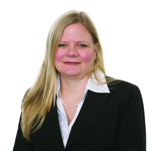 A smiling woman with blond hair wearing a black suit jacket over a white blouse with a pearl necklace.