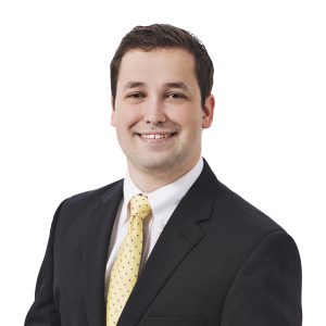 A smiling person wearing a suit with a white shirt and yellow tie.