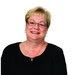 A smiling woman with short blonde hair, glasses, and a black top, set against a white background.