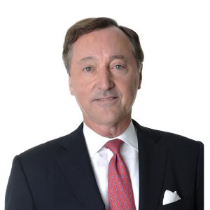 A man in a suit with a red tie and pocket square is smiling at the camera.
