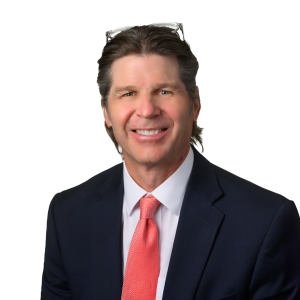 A smiling individual wearing a black suit, white shirt, and red tie poses against a white background.