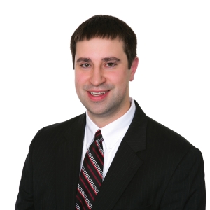 A smiling individual dressed in professional attire with a suit and striped tie against a white background.