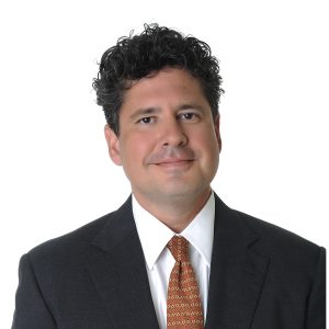 A person with curly hair wearing a suit and tie against a plain background.