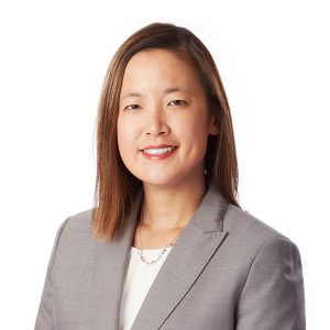 A professionally dressed individual is smiling against a white background.