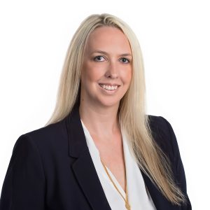 A smiling woman with long blonde hair wearing a dark blazer over a white top against a white background.