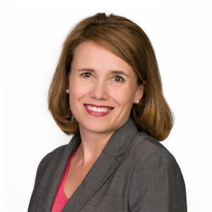 A smiling woman with shoulder-length hair wearing a grey blazer and a pink blouse.