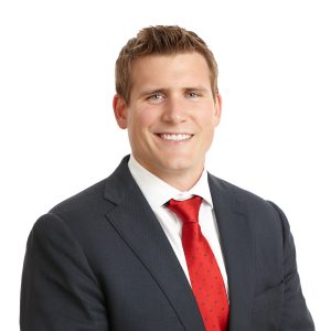 A smiling individual in a dark suit and red tie.