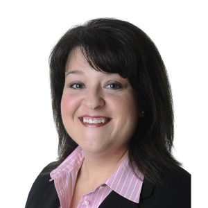 A smiling person wearing a pink-striped shirt and a black blazer.