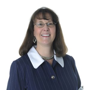 A smiling woman wearing a pinstriped blazer with a white collar and a necklace.