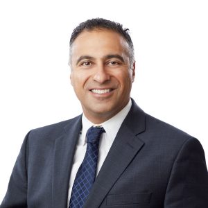 A smiling individual wears a suit and tie against a white background.