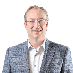 A smiling individual wearing glasses and a patterned blazer over a collared shirt.